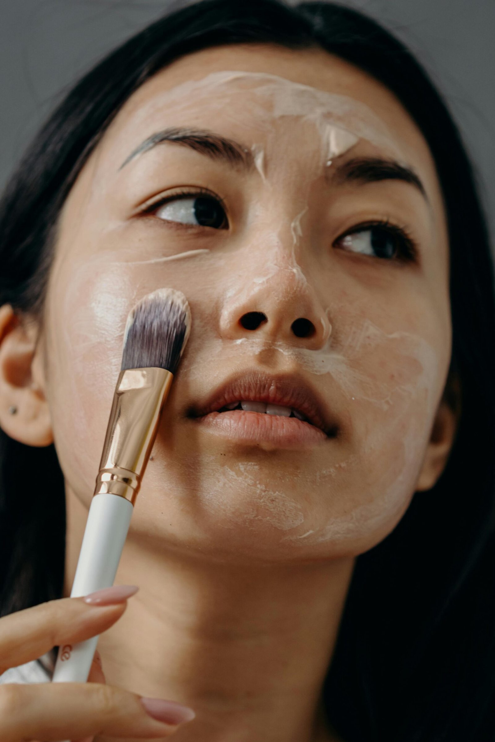 Close-up of a woman applying a face mask using a brush for skincare routine.